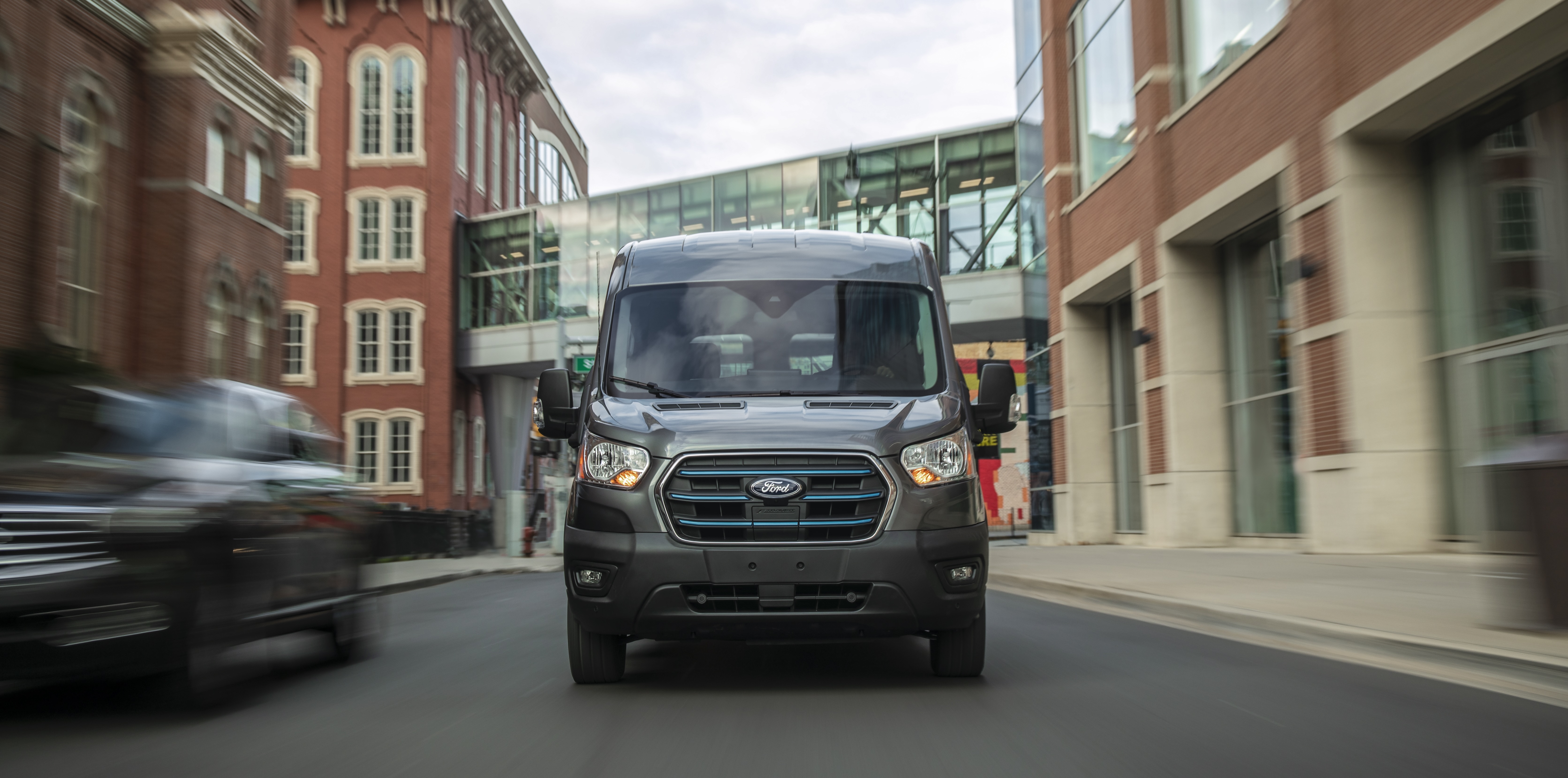  A silver E-Transit™ van being driven down a city street